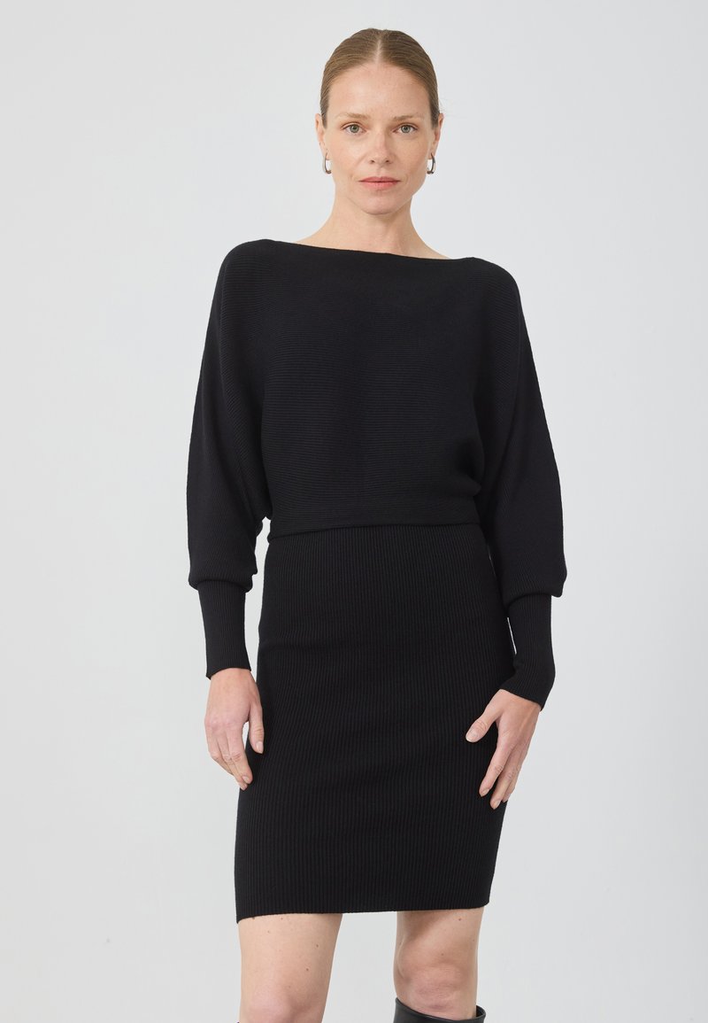 Rochie tricotată neagră, cu un decolteu larg, mâneci lungi și textură cu nervuri. Siluetă ajustată cu o lungime până la genunchi.