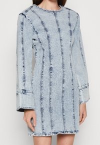 Džínové šaty s dlouhými rukávy, světle modré barvy, s vertikálními švy a zaobleným výstřihem. Tkanina má textura.