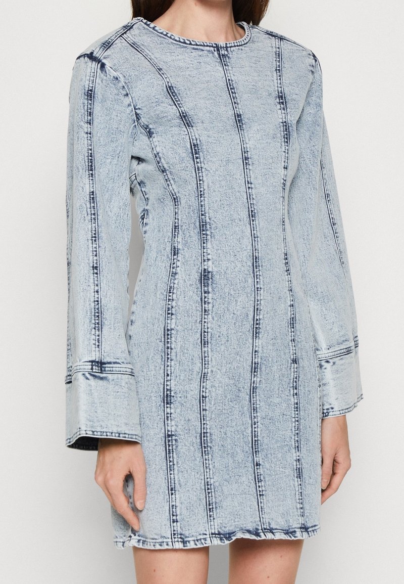 Džínové šaty s dlouhými rukávy, světle modré barvy, s vertikálními švy a zaobleným výstřihem. Tkanina má textura.