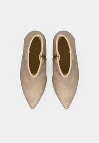 Botas de tobillo de ante beige con punta afilada y cremallera lateral. El interior cuenta con un forro en tono marrón claro, lo que enfatiza un diseño elegante y suave.