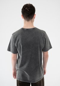 Gray cotton t-shirt with a faded, distressed texture, short sleeves, and a round neckline, displayed from the back on a plain background.