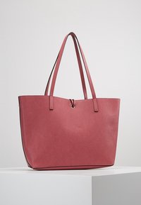 Różowa torba na ramię z imitacji skóry, z dwiema rączkami, otwartym wnętrzem i gładką teksturą. Posiada subtelną poświatę i minimalistyczny design.