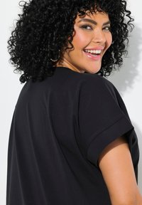 Musta lyhythihainen paita, jossa on rento istuvuus ja käännetyt hihat. Paidassa on sileä rakenne ja pyöreä pääntie.