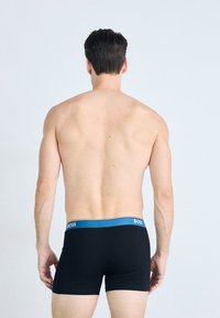 Black boxer shorts with a blue waistband featuring the "BOSS" logo, shown from the back on a person with short hair against a light background.