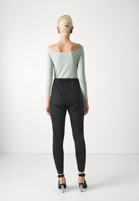 Top lungo a maniche lunghe verde menta scollato sulle spalle abbinato a pantaloni neri aderenti a vita alta e sandali neri con tacco con hardware decorativo.