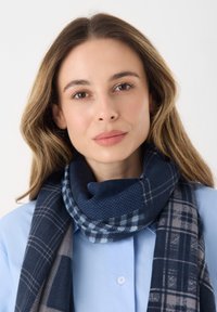 Écharpe bleu marine avec un motif texturé, présentant à la fois des designs à carreaux et en tartan, superposée sur une chemise bleu clair.
