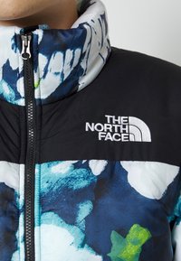 Chaqueta North Face con un cuerpo negro y un estampado floral en azul y verde multicolor, cuello alzado y cremallera frontal. Logotipo en el pecho.