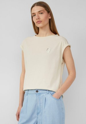 T-shirt crème, à manches courtes avec des poignets roulés ; présente un petit motif brodé sur la zone gauche de la poitrine ; tissu doux et léger.