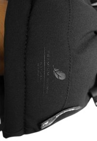 Schwarzer Premium-Daunenjackenstoff mit glatter Textur, geprägt mit Markenlogo und einem Etikett für natürliche Wärme. Sichtbare Nähdetails.