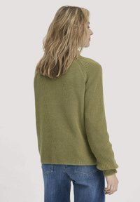 Groene gebreide trui met een casual pasvorm, geribbelde boorden en een ronde hals. Draagt over blauwe spijkerbroeken, waarbij een geweven stof wordt getoond.