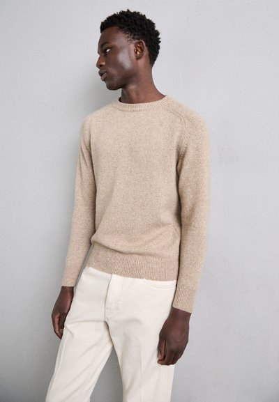 Suéter de punto texturizado beige con cuello redondo y puños acanalados, combinado con pantalones de color claro. Diseño simple, sin patrones ni acentos.