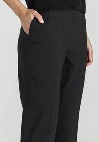 Czarne spodnie o dopasowanym kroju, z bocznymi kieszeniami, gładką teksturą i czystymi liniami. Odpowiednie zarówno do stylizacji casualowych, jak i profesjonalnych.