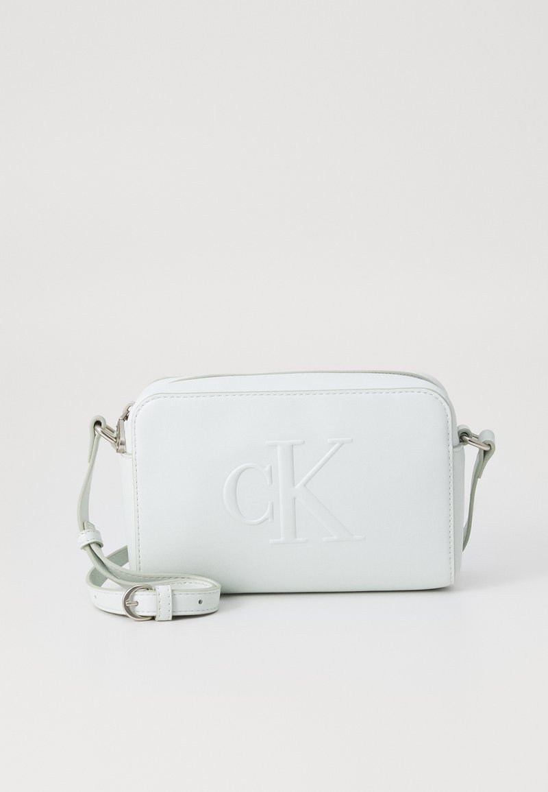 Ljusgrön läder crossbody-väska med ett präglat "cK"-logo, dragkedjestängning och justerbar rem. Slät yta och rektangulär form.