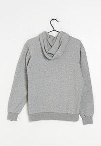 Felpa grigia con cappuccio, maniche lunghe, realizzata in tessuto morbido. Presenta una vestibilità standard e polsini e orlo a coste. Appesa a un gancio nero.
