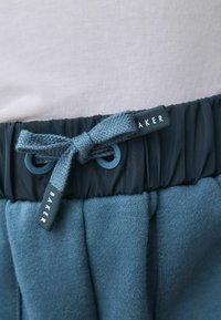 Blauwe sweatpants met een elastische tailleband, koordsluiting en een gladde textuur. Heeft een "BAKER" label nabij de verstelbare strik.