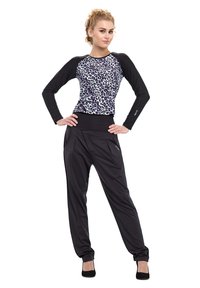 Top nero a maniche lunghe con design a stampa leopardata e pantaloni neri dal taglio rilassato con pieghe laterali. Scarpe nere completano il look.