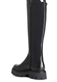 Botas negras hasta la rodilla con un frente de cuero brillante, parte trasera de textil mate, cremallera lateral y suela de goma texturizada y gruesa.