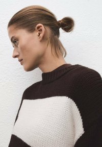 Jersey de punto grueso en marrón oscuro con una gran franja horizontal blanca. Presenta un cuello alto y una tela texturizada.