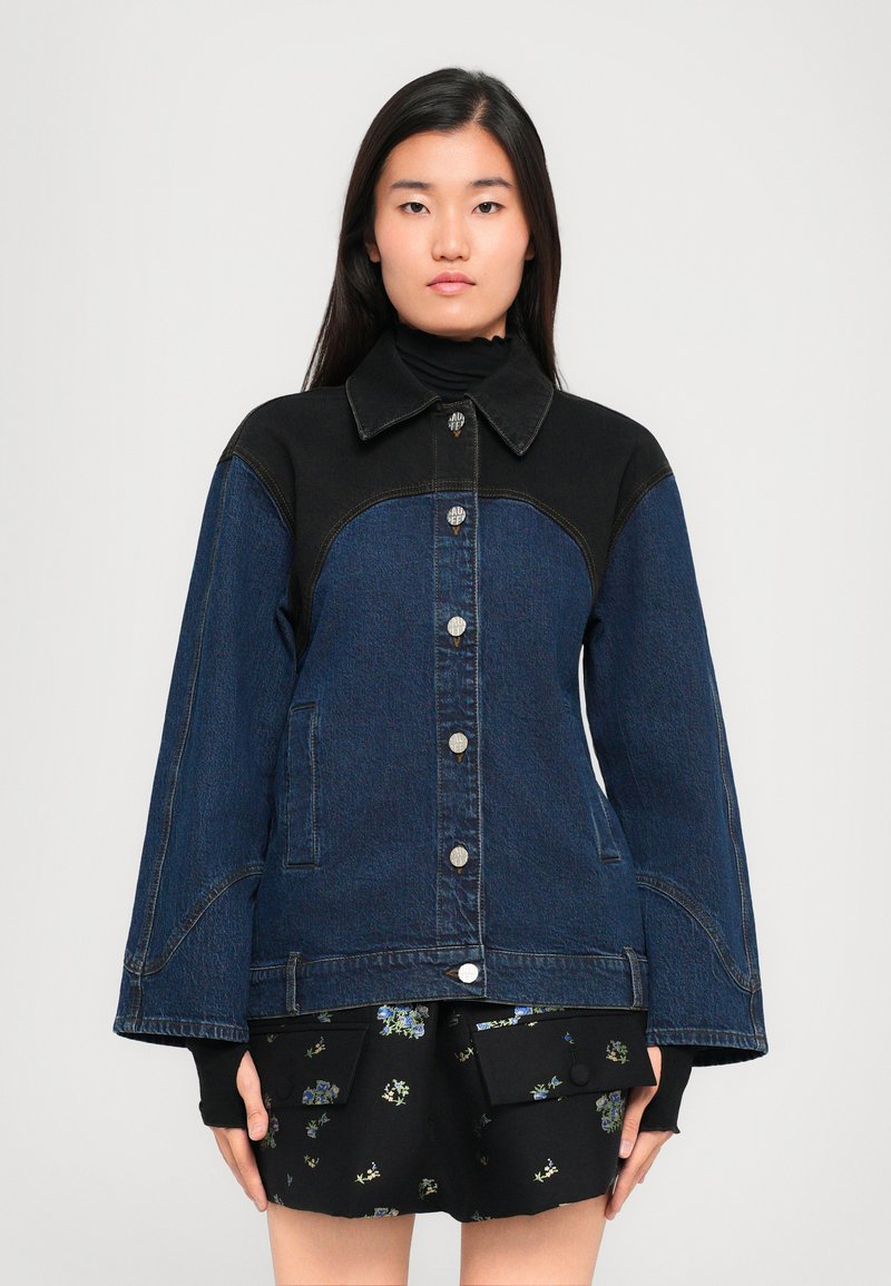 Jeans jakna s tamnoplavim tijelom i crnim ovratnikom, sadrži srebrne gumbe, bočne džepove i rukave u obliku zvona.