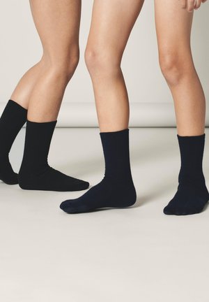 Schwarze und marineblaue Baumwollsocken in Knöchelhöhe, präsentiert an nackten Beinen. Die Socken haben eine glatte Textur und ein einfaches, klassisches Design.