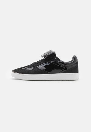 Black sneaker with a combination of smooth patent leather and textured suede. White rubber sole, black laces, and logo detail on the side.