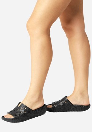 Sandales noires en caoutchouc texturé avec des découpes circulaires, un design à bout ouvert et une semelle striée pour une bonne adhérence et un confort optimal.