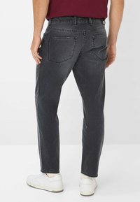 Jeans in denim grigio visti da dietro. Le caratteristiche includono una vestibilità rilassata, design a cinque tasche e cuciture a contrasto. Da abbinare a sneakers bianche.