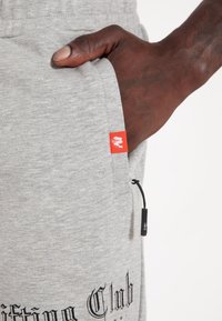 Grijze sweatpants met een elastische tailleband, trekkoorddetail, zijzak en een rood logotag; heeft een zwart tekstontwerp op het been.