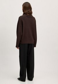 Donkerbruin gebreide trui met een kraag, oversized fitting en ribbelstructuur, gecombineerd met losse zwarte broek.