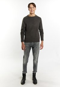 Maglione a maglia grigia scura con polsini e orlo a costine, abbinato a jeans grigi chiari e stivali neri con lacci. Design semplice e aderente; senza motivi.