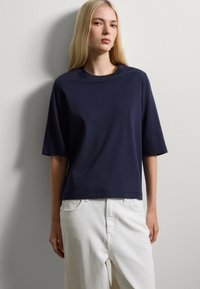 Korte mouwen navy blauwe T-shirt gemaakt van zachte stof, met een relaxte pasvorm en ronde hals, gecombineerd met witte hooggetailleerde broek.