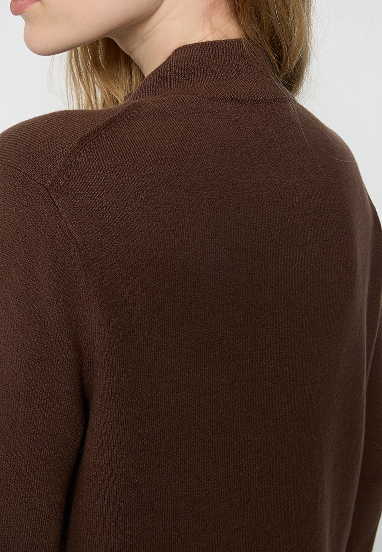 Brauner Strickpullover mit hohem Kragen und weicher Textur. Das Design umfasst einen nahtlosen Rücken und leichte Rippungen am Kragen.