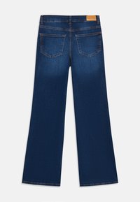 Jeans de boca de sino azul-escuro com uma textura suave, dois bolsos traseiros e um patch de couro castanho na cintura.