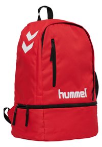 Rød rygsæk lavet af slidstærkt stof med et stort hovedrum, sidelommer, en sort lynlås og hvidt Hummel-logo med chevron-detaljer.