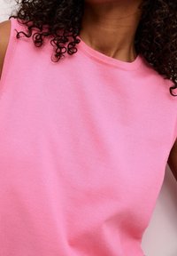 Różowy bezrękawnik z okrągłym dekoltem, wykonany z miękkiego materiału. Tekstura jest gładka, a szwy proste, bez dodatkowych zdobień.