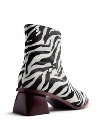 Botas tobilleras con patrón de cebra, hechas de un material suave, que presentan un tacón de madera en bloque y una forma afilada, con un acabado suave en blanco y negro.
