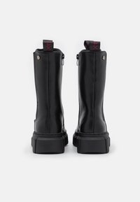 Botas de tobillo de piel negra con un acabado suave, que presentan una suela gruesa, cremalleras laterales y lengüetas con acentos rojos en la parte superior.