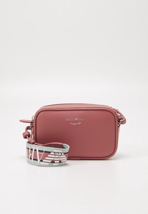 Pequeño bolso bandolera rosa texturizado con cremallera plateada y amplia correa de tela con marca, apoyado al frente sobre fondo blanco.