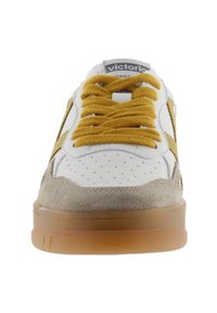 Sneaker bianca con lacci gialli e dettagli in suede, dotata di punta perforata, suola in gomma e logo sulla linguetta. Forma piatta e tondeggiante.