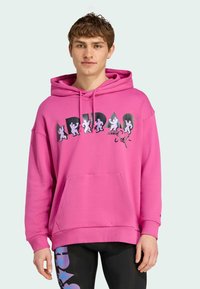 Lyserød hættetrøje med lomme foran, der har kontrastgrafik i sort og hvidt. Stoffet ser blødt ud, med et afslappet design og løs pasform.