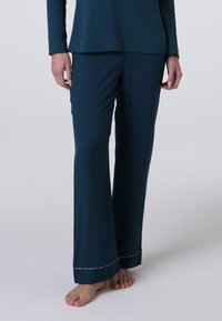 Pantaloni del pigiama verde acqua realizzati in un tessuto morbido, con una vestibilità ampia, gambe svasate e una cucitura decorativa lungo l'orlo. Posizione a piedi nudi.