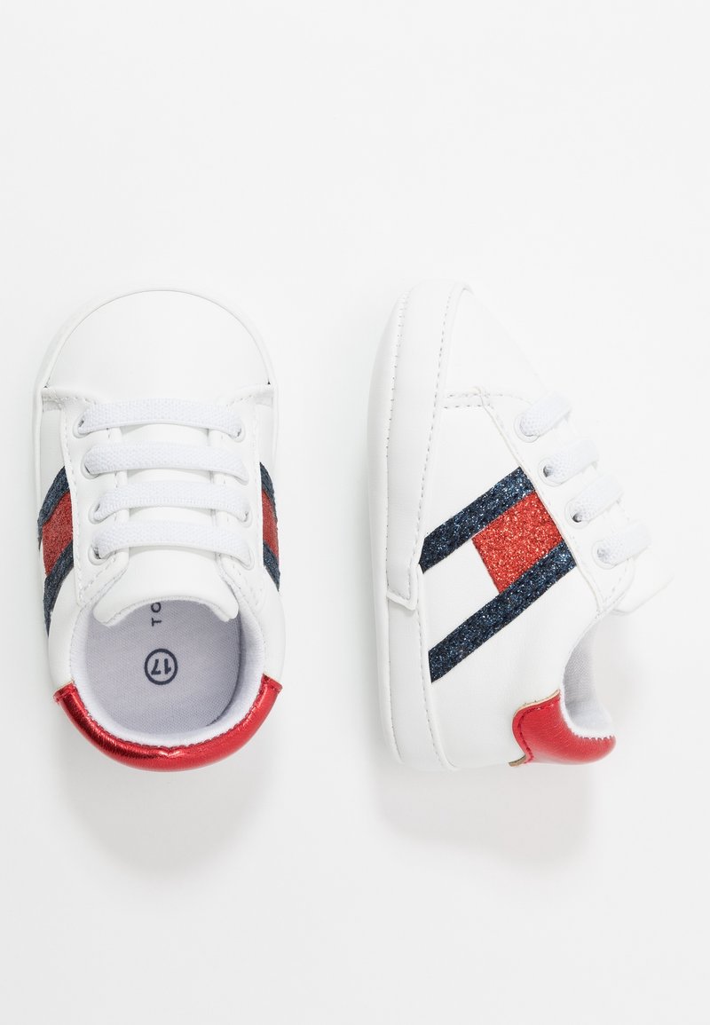 Zapatillas blancas con rayas brillantes en rojo y azul marino, punta redonda y cierre de cordones. Cuenta con un detalle brillante rojo en el talón y un forro interior suave.