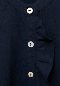 Tessuto blu navy con bordo arricciato e quattro bottoni rotondi. I bottoni sono realizzati in materiale chiaro con piccoli fori.