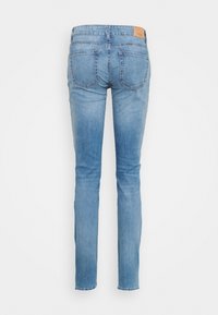 Jeans de mezclilla azul claro con un corte ajustado, que cuentan con dos bolsillos traseros y un parche de cuero en la cinturilla. Textura suave y diseño clásico.
