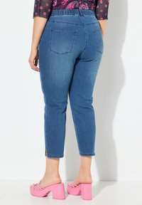 Siniset farkut korkealla vyötäröllä, kapea malli, lyhyt pituus ja sivuhalkiot helmassa, yhdistettynä vaaleanpunaisiin paksupohjaisiin sandaaleihin.