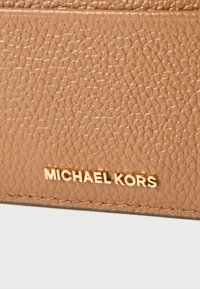 Portafoglio in pelle testurizzata color cuoio con logo dorato "MICHAEL KORS". La superficie presenta una trama a grana grossa con dettagli di cuciture visibili.