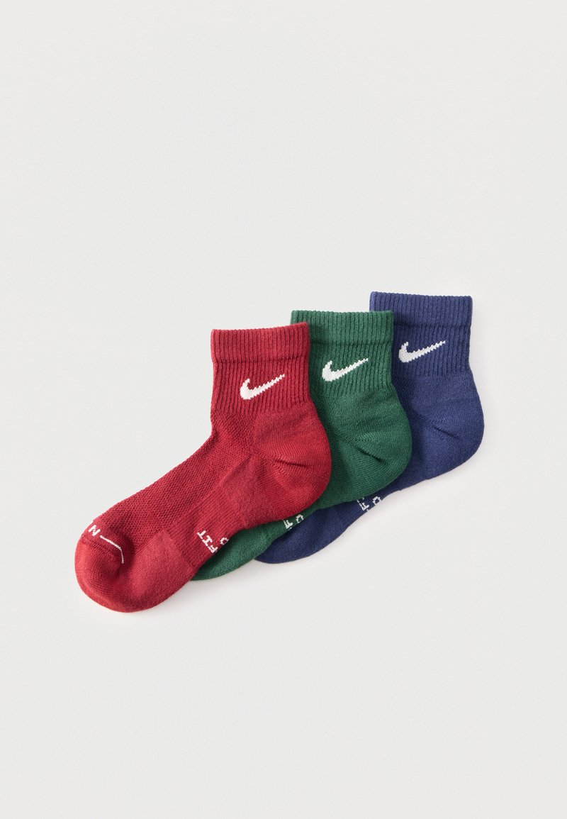 Τρεις κάλτσες αστραγάλου Nike σε κόκκινο, πράσινο και μπλε, τοποθετημένες αλληλεπικαλυπτόμενες σε απλό λευκό φόντο.