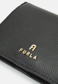 Portefeuille en cuir noir avec une surface texturée. Présente un logo doré "FURLA" affiché de manière proéminente. Les bords et les coutures sont propres et bien visibles.