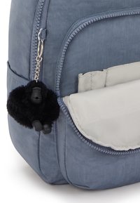 Zaino in tessuto blu con una tasca grigia e un portachiavi di gorilla peloso nero attaccato alla cerniera per un tocco in più.