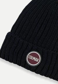 Pletena mornarsko modra kapa z rebrasto teksturo in okroglo oznako Colmar v maroon in beli barvi, prišito na sprednji strani.